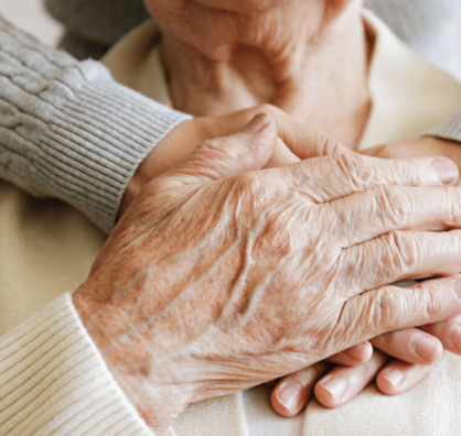 close up of old couples hands - the woman's hand is placed over the mans hand.