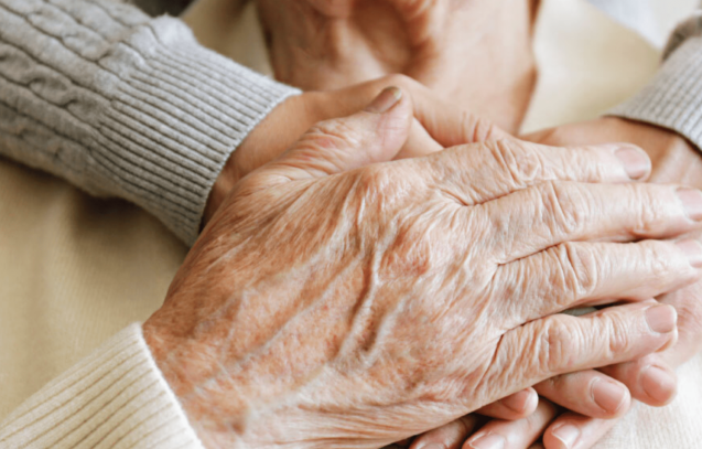 close up of old couples hands - the woman's hand is placed over the mans hand.