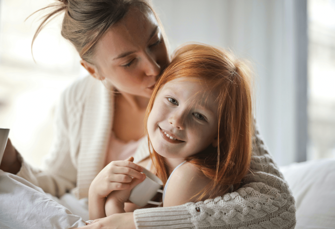 Mother and daughter sitting on a couch. the mother is kissing her daughter on hear head.